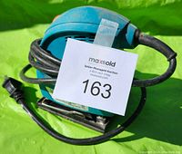 Teal blue electric palm sander with attached power cord, showing the top handle grip and sanding base, front view outdoors on a green background with seller auction tag