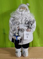 Front view of large white Santa figurine standing about 25 inches tall, holding silver wrapped gift and silver mini tree.
