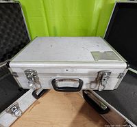 Closed aluminum metal tool case with black handle and silver clasps, showing surface scuffs and scratches.