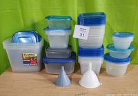 Photo showing a variety of plastic food storage containers in different sizes and styles with blue and gray lids, alongside two plastic funnels (blue and white).