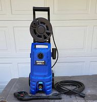 Full frontal view of blue Simoniz power washer unit with attached hose, pressure gun, and hose reel on top.