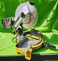 Mitre cutoff saw viewed from the left side showing yellow metal base, black dust collection bag and semi-transparent blade guard.