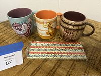 Three Disney character mugs and a set of sealed straws on a wooden surface.