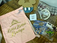 Pink cloth bag with gold lettering and Mickey Mouse shaped leash holder with white pegs, plus other items on wooden surface