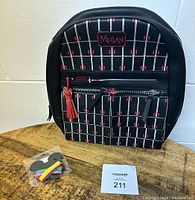 Front view of new black Disney Mulan backpack with red accents on wooden table, small pack of Disney hair ties, and inventory card.