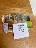 Five Pokémon cards fanned out on wooden surface with visible holographic effects and Japanese and English text.