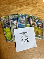 Five Pokémon cards displayed in protective sleeves on a wooden surface, showing some of the individual cards.