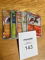 Front view of five Pokémon cards in protective sleeves, showing artwork of Hawlucha, Yoropon and others, with holographic and reverse holo effects.