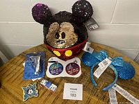 Photo showing a black and purple flip sequin Mickey Mouse ear plush, blue glitter Minnie Mouse ears headband, Disney marathon buttons, Mickey Mouse magnet and keychains arranged on a table.