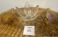 Front view of crystal flower petal textured glass bowl flanked by two amber carnival glass diamond-shaped dishes, all displayed on wooden surface.