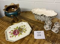 Full view of urn, pair of candle holders, and floral tin tray on wooden table.