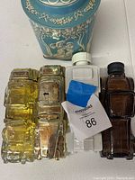 Photo showing four vintage Avon bottles, three made of glass in yellow and amber tones and one made of white plastic, all with distinct shapes.