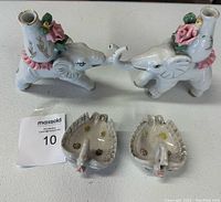 Two ceramic elephant candlesticks with raised trunks and floral decorations alongside two small leaf-shaped ceramic swan trinket dishes with flower motifs.