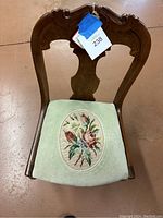 Front view of the vintage wooden chair showing its carved backrest and floral needlepoint seat.