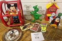 Photo showing the collection of vintage Disney toys including Mickey Mouse figure in cage, acrylic figures, clock, and 101 Dalmatians related items on wood surface.
