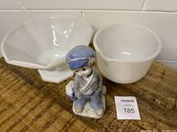 Photo showing the two white glass bowls and ceramic boy figurine arranged on a wooden surface against a white brick wall