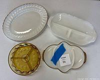 Four vintage glassware items on white surface: clear glass oval platter, white divided dish with gold trim, amber divided dish, and white dish with gold trim