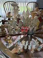Overview on glass table showing varied cherub and angel statues including white plaster and porcelain pieces, glass angels, and painted figurines.