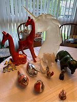 Overview of 14 assorted animal figurines on a table including unicorn head, giraffes, buffalo, camels, birds, swan and glass fish.