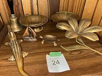 Photo showing all brass items arranged on wooden shelf including alligator nutcracker, turtle figurine, handbell, sailboat, bowls, and flower figurine.