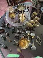 Photo showing wide assortment of brass and metal antique hardware and figurines on glass table