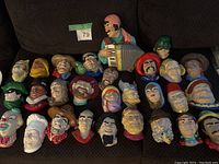 Photo of 29 assorted ceramic head sculptures arranged on a dark surface, showing a variety of characters and colorful designs.