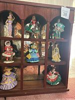Full view of the wooden display shelf with eight ceramic ladies figurines seated in its compartments