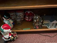 Shelf view of ceramic Santa and snowman figurines, decorated tins, and glass jar