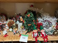 Wide view showing multiple Christmas-themed decorations including a small decorated tree, elf figurines, 'Merry Christmas' sign, candy cane, floral branches, and other assorted figurines.