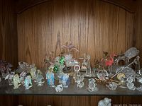 Glass animal figurines including dolphins, penguins, fish, turtles, flamingos, koalas, and floral decor displayed on wooden shelf.