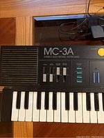 Close-up image of the upper left area of the keyboard showing MC-3A branding, speaker grill, and volume sliders.