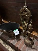 Photo showing the fireplace fan, scuttle bucket, and etched coffee pot arranged on a brick hearth.