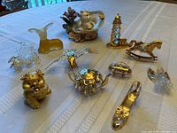 Overview of all 11 decorative miniature figurines displayed on a white tablecloth. Items include animals, a teapot, a rocking horse, and other ornamental pieces.