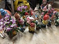 Wide shot showing a large assortment of colorful garden gnomes, some holding flowers and others with pointed hats.