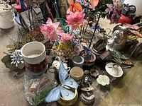 Overview of garden decor including ceramic pots, metal flower stakes, artificial flowers, and garden statues arranged on floor.