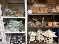 Photo showing multiple shelves with deer statues (large and small), raccoons, skunk statues, wave planter, owl planter, and decorative lanterns.