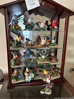 Full view of dark wood display cabinet with four glass shelves containing eight porcelain figurines and two figurines on base