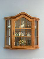 Full view of oak wall-mounted glass display cabinet with arched top and side windows containing porcelain figurines.