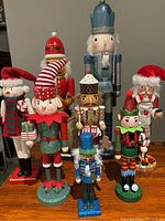 Overview photo of all eight nutcracker and elf figurines arranged on a wooden surface showing a variety of festive holiday designs and colors.