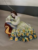 Side angle showing the woman reclining with an open book on a blue cushion on a brown and yellow couch. The floral pattern on the dress is visible.