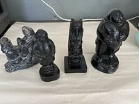 Four soapstone sculptures including human figures and a totem pole, displayed on a white cloth background.