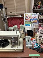 Overall view of sewing machine, carrying case, scissors, quilting templates, and craft supplies arranged on table.