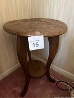 Side view of the round wooden side table showing hand-carved details on the legs and lower shelf.