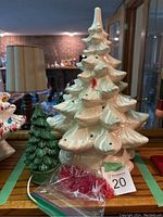 White ceramic Christmas tree with red bird bulbs in front, smaller green ceramic tree beside it on a wooden surface