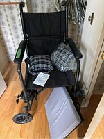 Front view of black manual wheelchair showing seat, armrests, detachable footrests, and two black and white plaid cushions on the seat.
