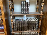 Wooden book case filled with leather-bound Encyclopedia Americana volumes, showing two shelves with books arranged upright and spines facing out.