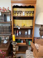 Front view of one wooden bookcase with scalloped top trim, holding silver goblets, collectibles, and other small items.