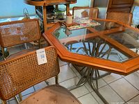 Photo of the dinette set showing the octagonal glass top table with wood trim and the four wicker back chairs with cane seats. Chair bottoms show visible stains as per seller note.