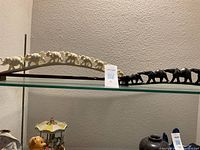 Two sets of elephant figurines displayed on a glass shelf, with a small tag showing the lot number. Light-colored elephants on a wooden curved base and black elephants lined up.