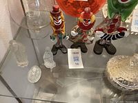 Photo of three colorful glass clown figurines on a glass shelf, smallest has broken foot.